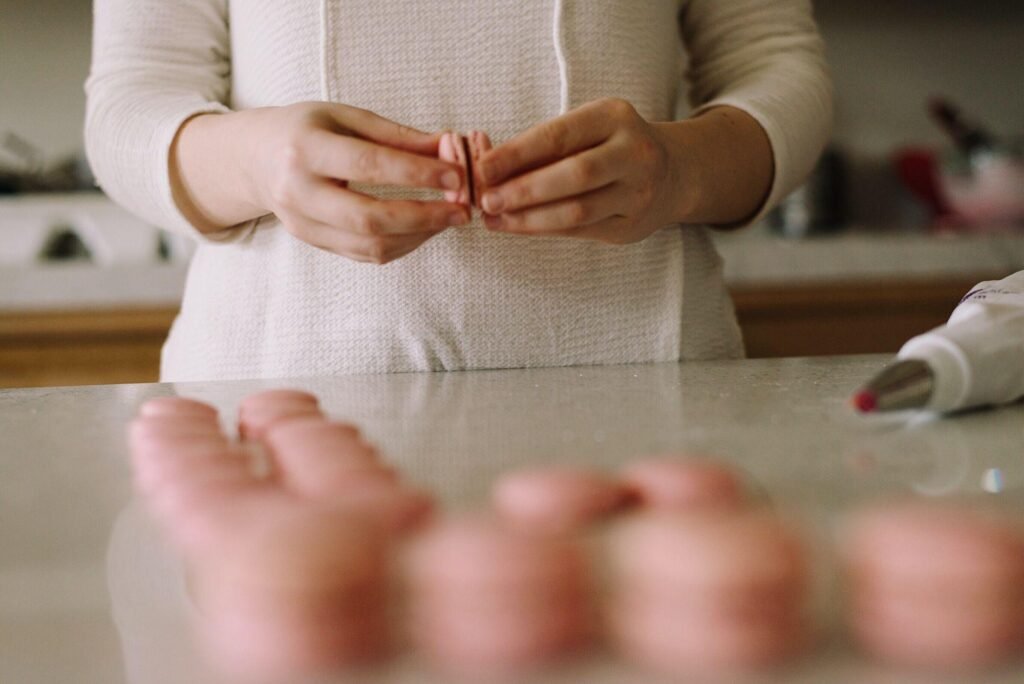 A person assembling pink macarons on a modern kitchen countertop, highlighting the joy of baking in custom Einbauküchen Tessin kitchen designs.
