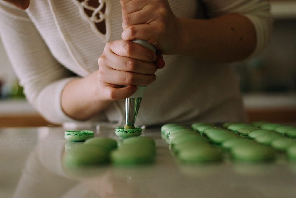 A person using a piping bag to fill green macarons on a clean kitchen countertop, highlighting the joy of baking in a modern Einbauküchen kitchen.