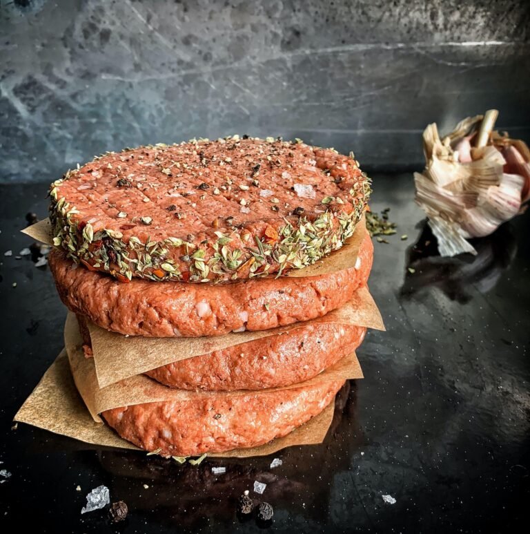 A stack of raw seasoned burger patties separated by parchment paper on a dark surface, perfect for cooking in modern Einbauküchen Tessin kitchens.