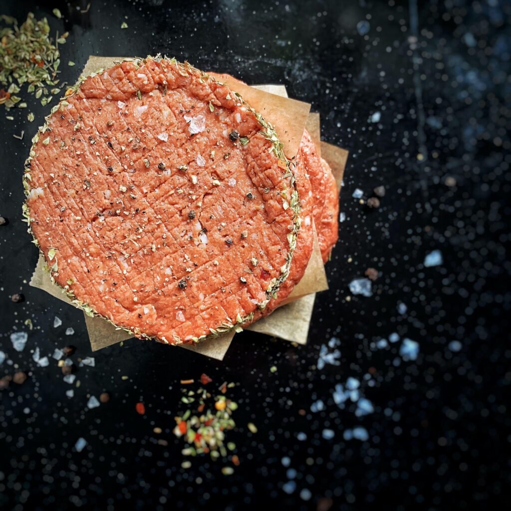 Raw seasoned burger patties stacked on parchment paper, ready for cooking in a modern Einbauküchen kitchen setting in the Rostock region.
