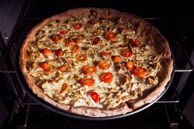 A freshly baked savory tart with mushrooms and cherry tomatoes on a baking tray inside a modern oven from a kitchen studio in Rostock.